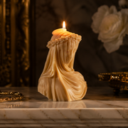 Decorative candle shaped like a draped figure on a marble surface with gold accents.