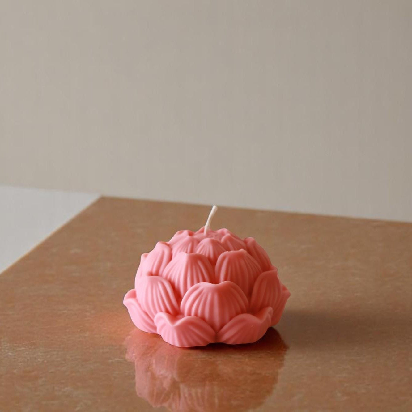 Pink lotus-shaped candle on a reflective surface with a neutral background