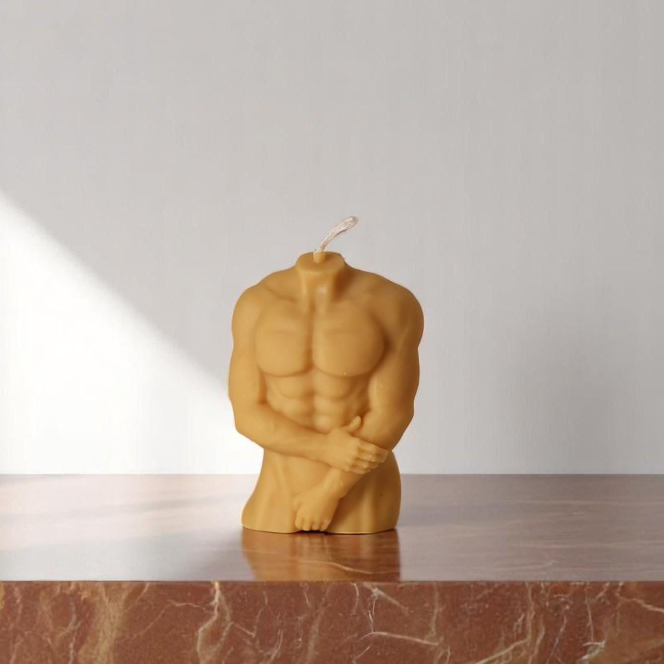Candle shaped like a muscular figure on a marble surface with a white background