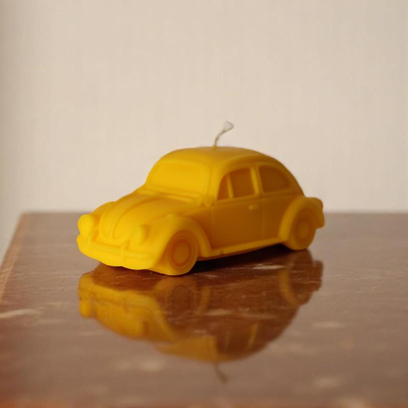 Yellow car-shaped candle on a reflective surface with a neutral background