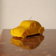 Yellow car-shaped candle on a reflective surface with a neutral background